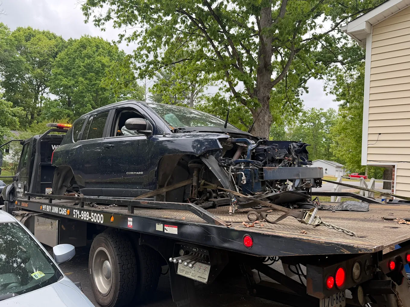 Damaged Jeep Compass loaded on a branded rollback tow truck during junk car pickup