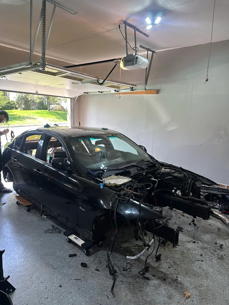 Stripped black BMW sitting in a garage with major parts removed before sale