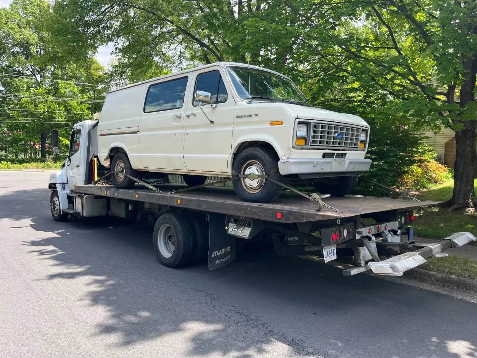 Older Ford Econoline van loaded onto a flatbed tow truck in Burke, VA
