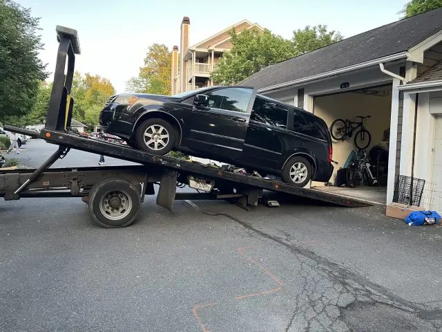 Black van being loaded onto a flatbed tow truck in a Northern Virginia apartment community
