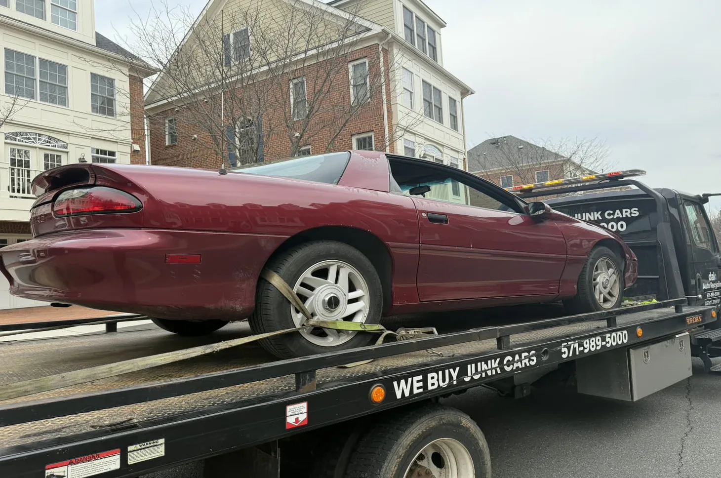 Older Camaro loaded onto a Dalo Auto Recycling flatbed truck in a Sterling townhome community